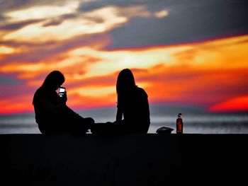 Silhouette person photographing by sea against sky during sunset