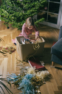 Girl searching ornaments in cardboard box sitting by christmas tree at home