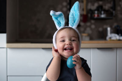 Cheerful laughing baby wearing blue bunny ears and holding blue easter egg. lifestyle, copy space