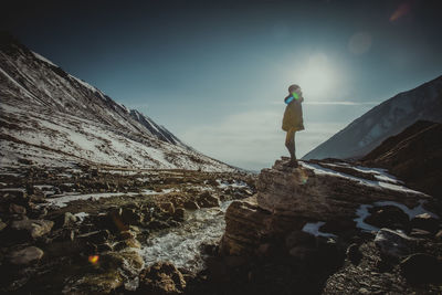 Man standing on rock by mountain against sky