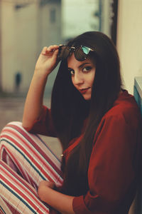 Model woman sitting against a wall wearing bourdeous shirt and stripes pant looking at camera