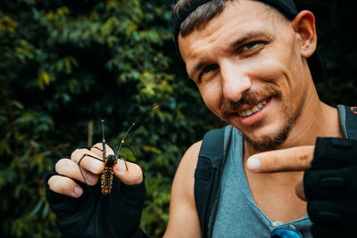 Portrait of man pointing at insect against plants