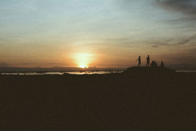 Silhouette people standing on beach against sky during sunset