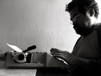 Side view of man using typewriter against wall