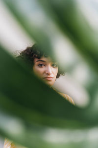 Young woman with blank expression seen through monstera leaf