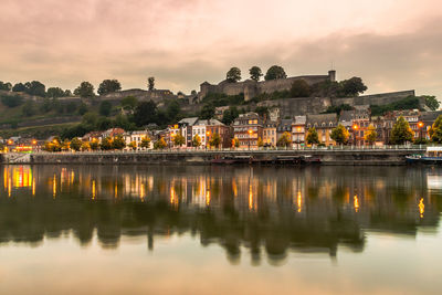 Scenic view of lake by buildings against sky at sunset