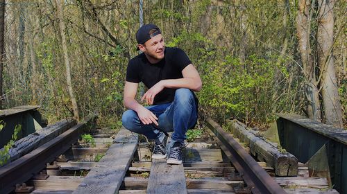 Young man crouching on wood against trees