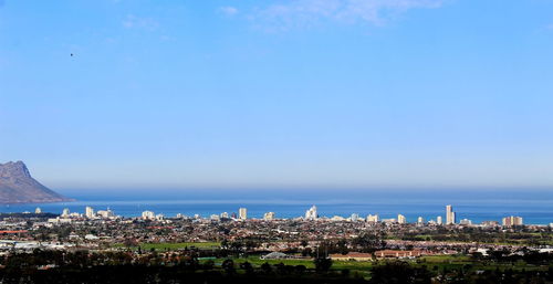 Aerial view of townscape by sea against blue sky