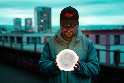 Portrait of man wearing hat standing against city in background