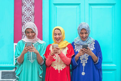 Smiling female friends using smart phones against building