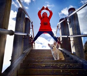 Low angle view of woman with dog standing on steps against sky