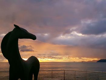 Silhouette statue by sea against sky during sunset