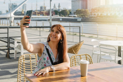 Portrait of young woman photographing with mobile phone in city