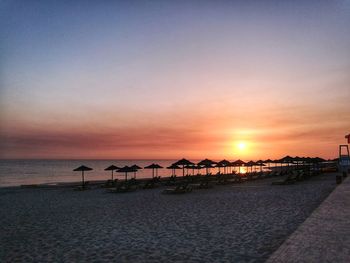 Parasols by deck chairs at beach during sunset