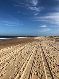 Tire tracks on beach against blue sky