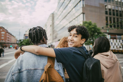Portrait of smiling teenage boy walking with arm around friend in city street