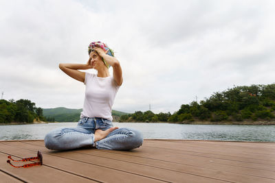 Woman sitting by lake against sky