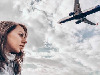 Low angle view of woman standing against plane flying in sky