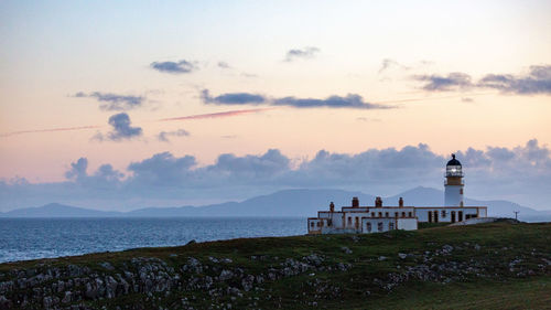 Lighthouse by sea against sky during sunset