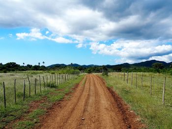 Dirt road amidst agricultural field against sky