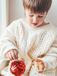 Kid with red ball for christmas tree. boy in cable-knit oversized sweater. new year outfit.