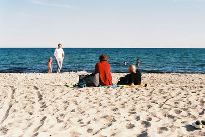 People sitting on beach against clear sky