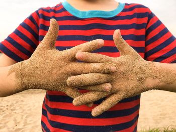 Midsection of boy with dirty hands clasped at sandy beach
