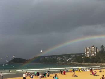 People on beach against rainbow in sky