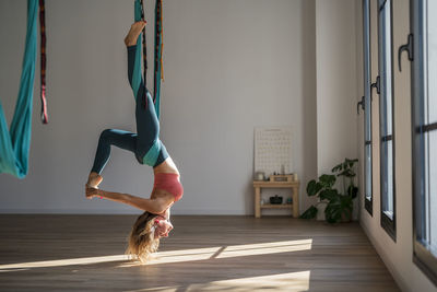 Woman hanging upside down on aerial silk practicing yoga at health club