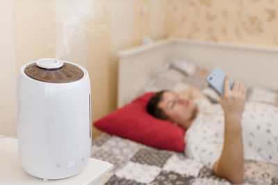 Humidifier spreading steam. humidification of dry air in sleeping room. on the background young man