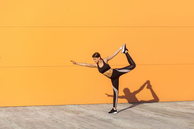 Woman with arms outstretched against orange wall