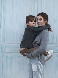 Portrait of daughter and mother standing against door