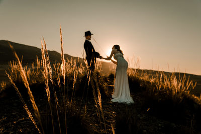 Friends standing on field against sky during sunset