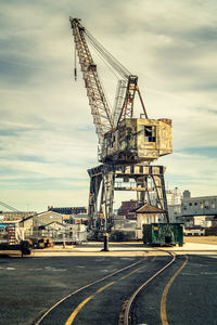 Cranes at construction site against cloudy sky during sunset