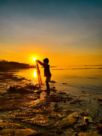 Silhouette man standing on beach against sky during sunset