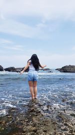 Rear view of woman standing at beach against sky