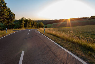 Road amidst field against sky during sunset