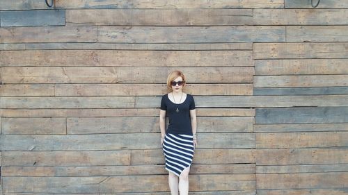 Young woman standing against wooden wall