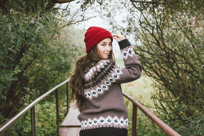 Woman wearing hat standing against trees during winter