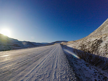 Road leading towards mountains against clear blue sky