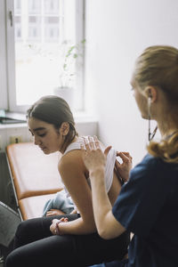 Female nurse examining girl using stethoscope in clinic