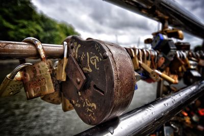 Close-up of padlocks hanging on metal by sea against sky