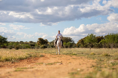 Man horse riding on land against sky