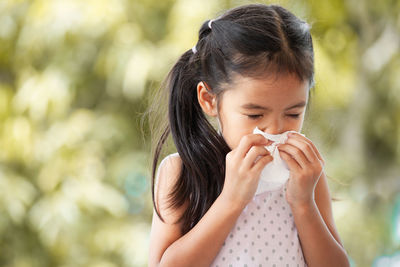 Close-up of girl sneezing nose while sitting outdoors