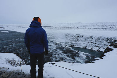 Rear view of man standing in sea against sky during winter