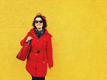 Young woman standing against yellow wall