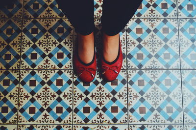 Low section of woman with red shoes standing on tiled floor