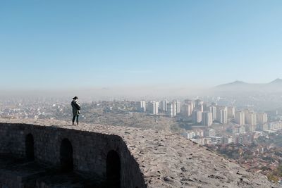 Woman standing on wall against cityscape and sky