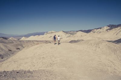 People walking on desert against clear sky