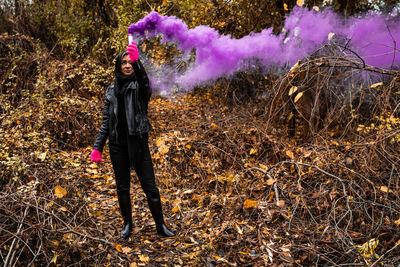 Young woman holding distress flare while standing in forest during autumn